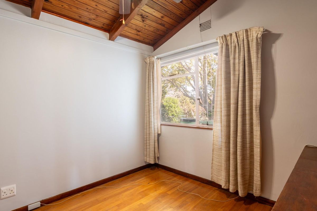 A bright bedroom featuring exposed timber ceiling beams, polished wooden flooring, and a large window providing natural light.