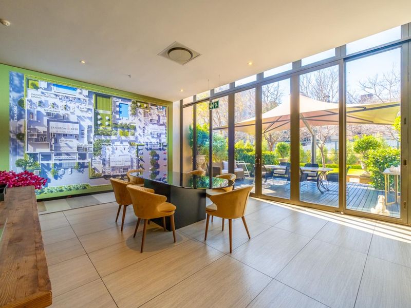 Modern clubhouse or reception area featuring large floor-to-ceiling glass doors opening onto a landscaped patio and garden space.