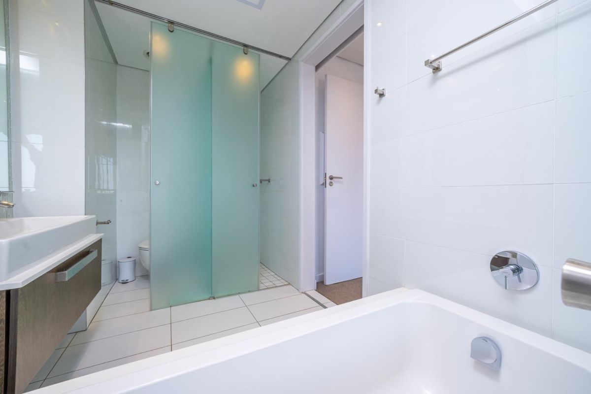 Modern bathroom featuring a white bathtub, wall-mounted vanity, and a separate glass-enclosed shower area with tiled flooring.