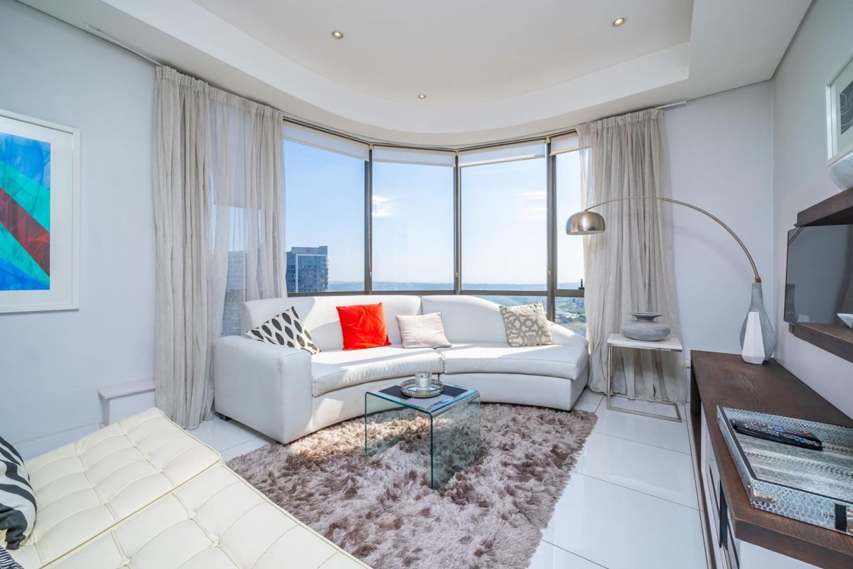 Modern living room featuring expansive floor-to-ceiling curved windows with panoramic city views, recessed ceiling lighting, and polished tile flooring.