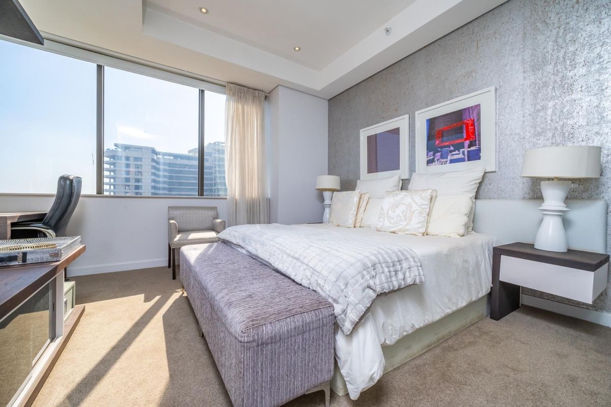 A well-lit bedroom featuring a large window with city views, recessed ceiling lighting, and a textured feature wall.