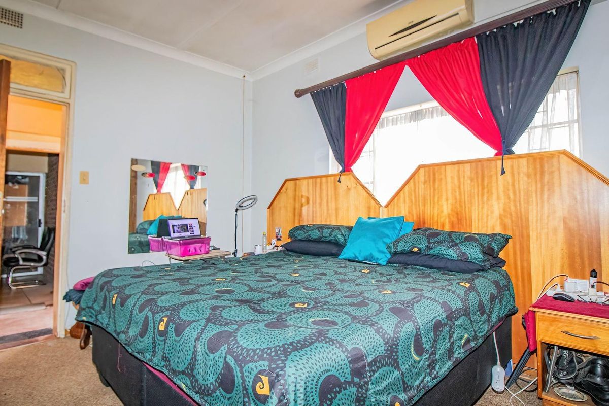 A bedroom featuring a built-in wooden headboard, wall-mounted air conditioning unit, and carpeted flooring.