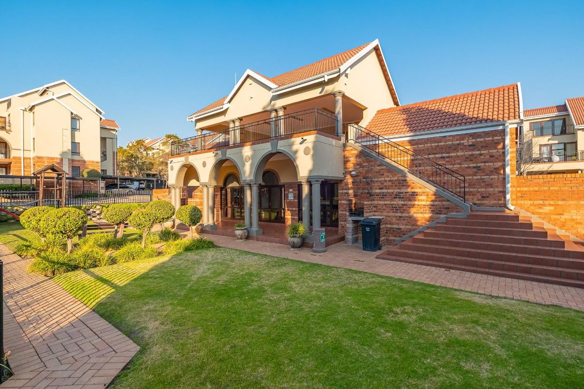 Rear view of a multi-story apartment building featuring a brick facade, arched ground-floor patio, upper-level balcony, and an external staircase leading to a landscaped garden.