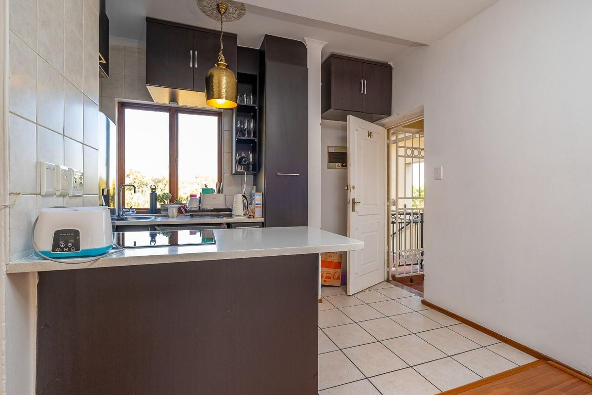 Compact kitchen featuring dark wood cabinetry, stone countertops, and tiled flooring, with direct access to an external security gate.