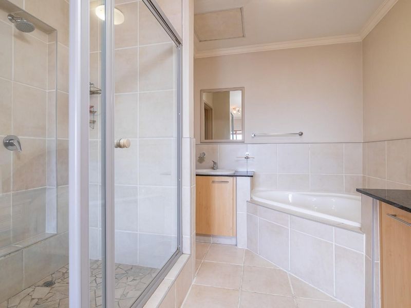 A well-maintained bathroom featuring a glass-enclosed shower, a built-in bathtub with tiled surround, and a vanity unit with a stone countertop.