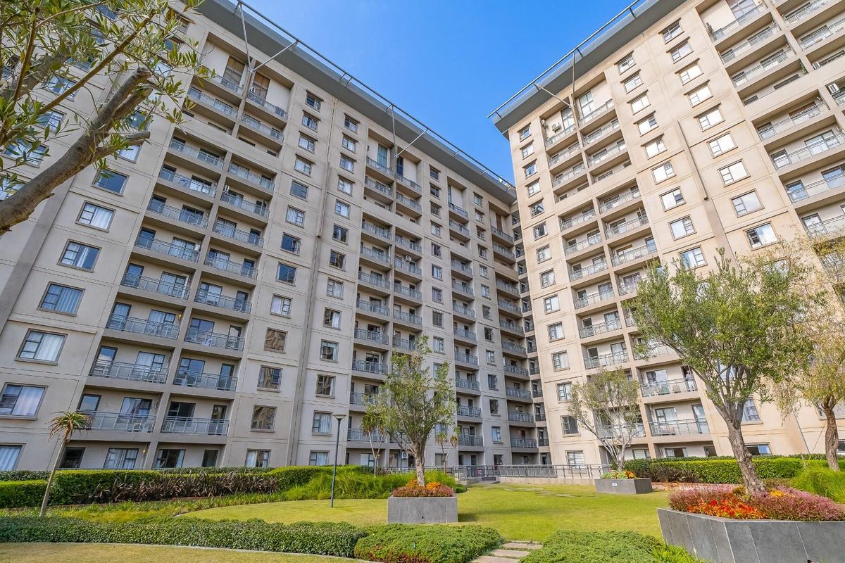 A low-angle view of a modern multi-story apartment complex featuring landscaped garden areas and private balconies for each unit.