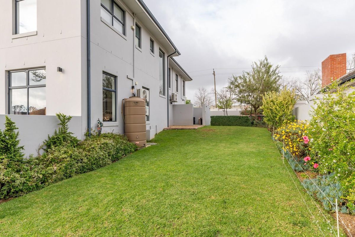A well-maintained rear garden featuring a lush lawn, established garden beds, and a side elevation of the house with a water tank.