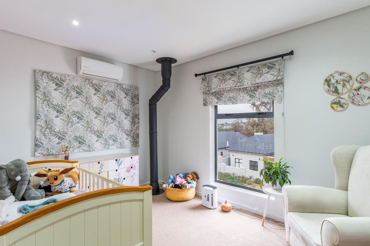 A well-maintained bedroom featuring a built-in air conditioning unit, a prominent flue pipe, and large aluminium-framed windows providing natural light.