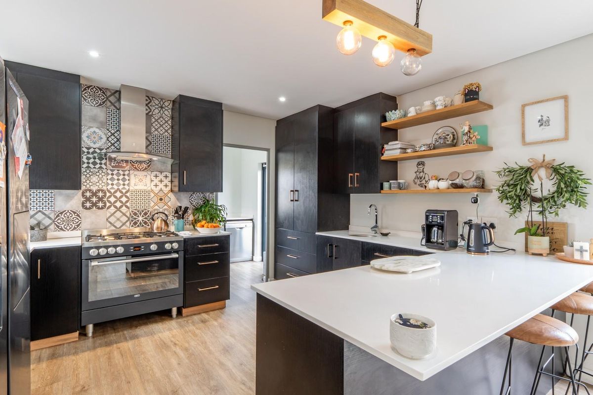 Modern kitchen featuring dark cabinetry, patterned tile backsplash, quartz countertops, and a central island with breakfast bar seating.