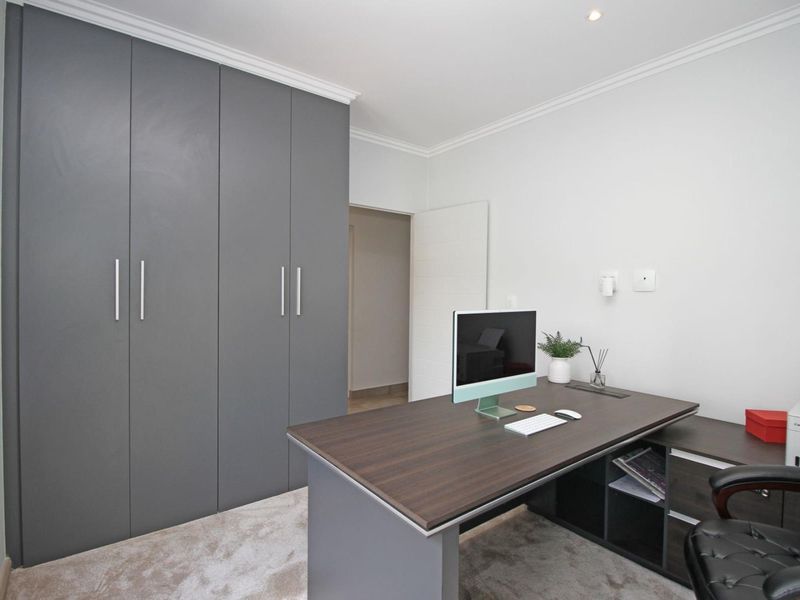 A well-maintained home office featuring modern grey built-in cupboards, neutral carpeting, and recessed ceiling lighting.