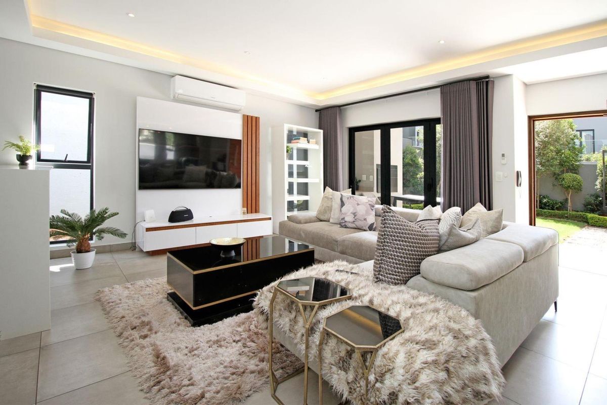 Modern, well-lit living room featuring tiled floors, a built-in media wall, split-system air conditioning, and large glass sliding doors opening to the garden.