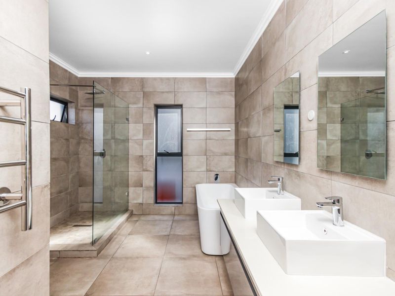 Modern bathroom featuring a double vanity, freestanding bathtub, walk-in glass shower, and neutral floor-to-ceiling tiling with a heated towel rail.