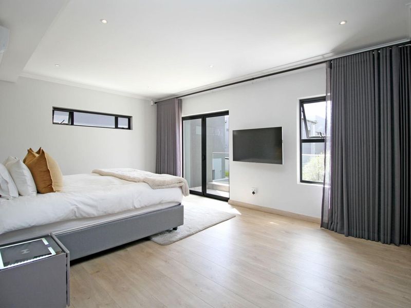 Spacious modern bedroom featuring light laminate flooring, recessed downlights, and direct access to a private balcony through sliding glass doors.
