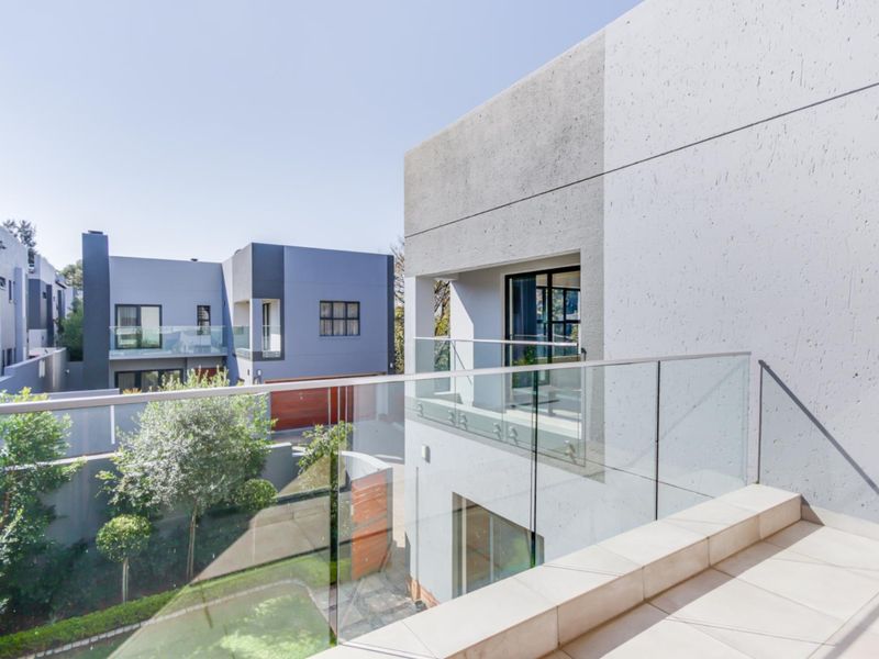 A modern, elevated balcony featuring a sleek glass balustrade and tiled flooring, overlooking the townhouse complex grounds.