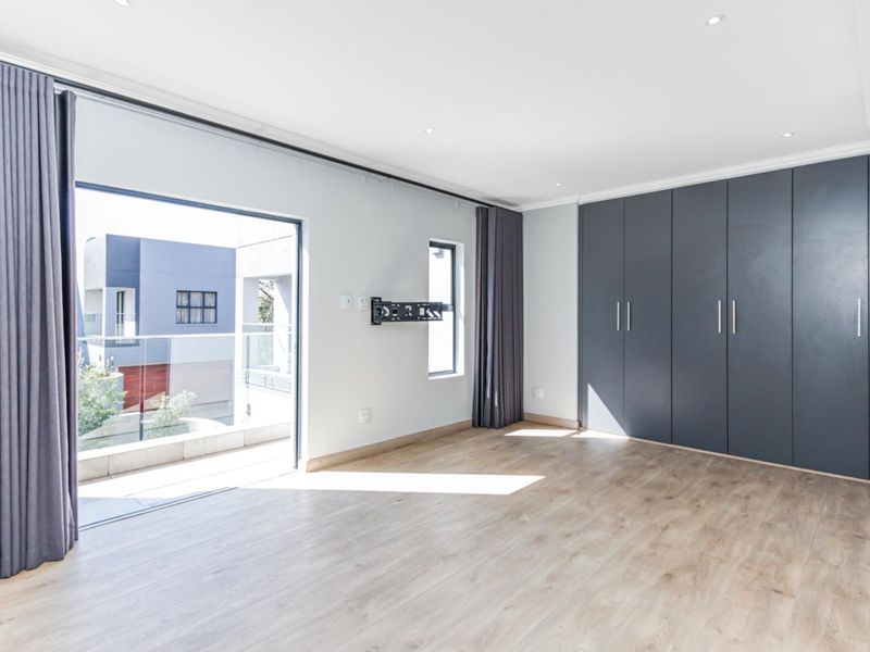 Spacious bedroom featuring modern laminate flooring, extensive built-in cupboards, recessed lighting, and direct access to a private balcony through a large sliding glass door.
