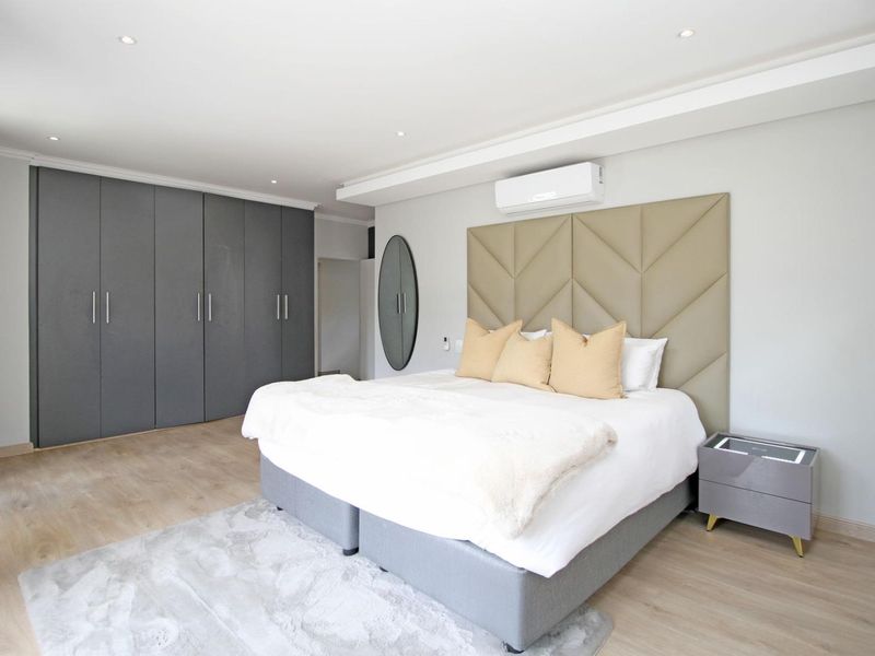 Modern bedroom featuring built-in cupboards, recessed lighting, and a wall-mounted air conditioning unit with light-toned laminate flooring.