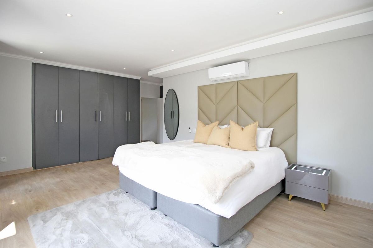 Modern bedroom featuring built-in cupboards, recessed lighting, and a wall-mounted air conditioning unit with light-toned laminate flooring.