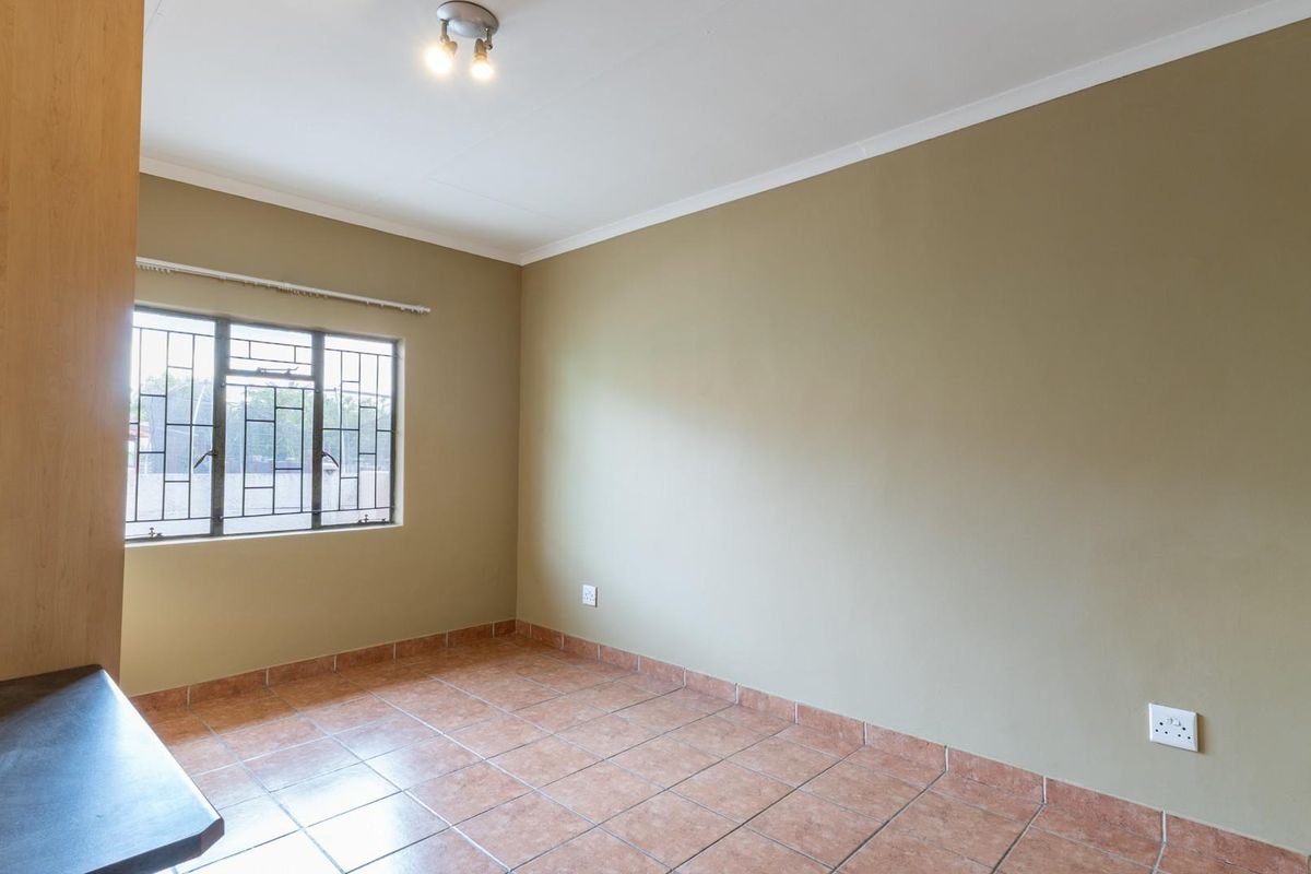 A vacant bedroom featuring tiled flooring, built-in cabinetry, and a window with security bars.