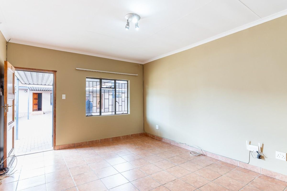 A bright, empty living room featuring tiled flooring, a security-barred window, and direct access to an outdoor courtyard area.