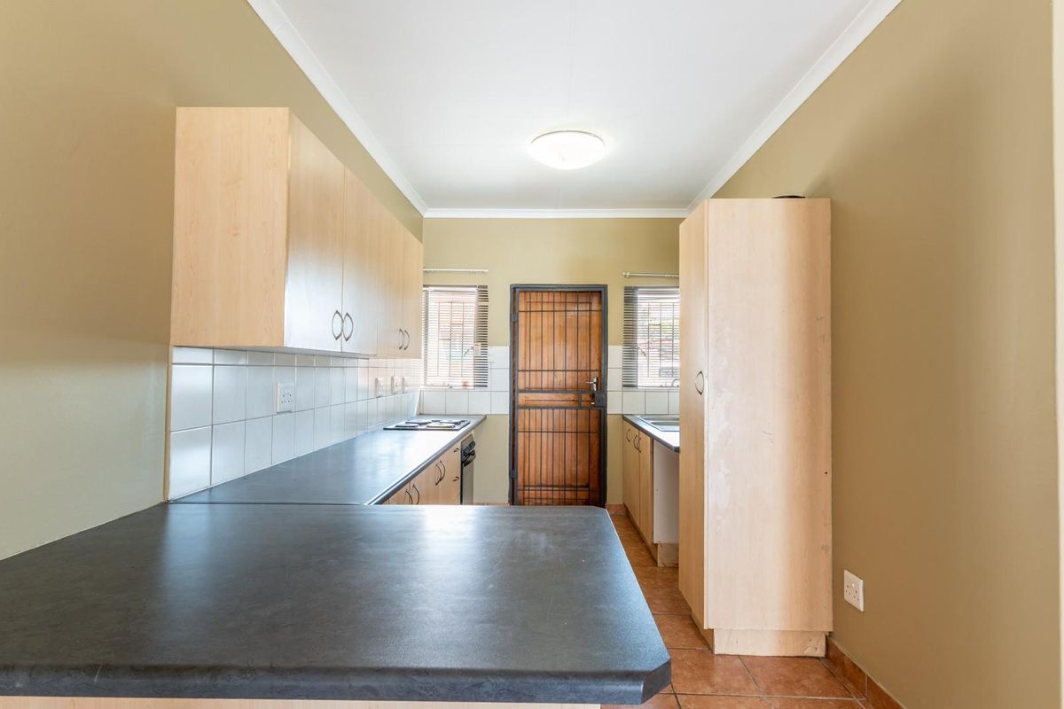 A functional kitchen featuring light wood-toned cabinetry, dark laminate countertops, tiled backsplash, and a rear exterior door with security gate.