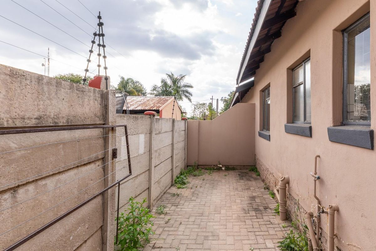 A narrow side courtyard featuring paved flooring, precast concrete boundary walling, and exposed exterior plumbing fixtures along the townhouse wall.