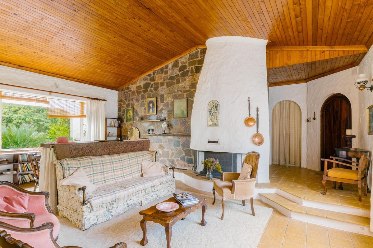 Spacious living room featuring a vaulted timber ceiling, a prominent stone-clad fireplace, and tiled flooring with a split-level layout.