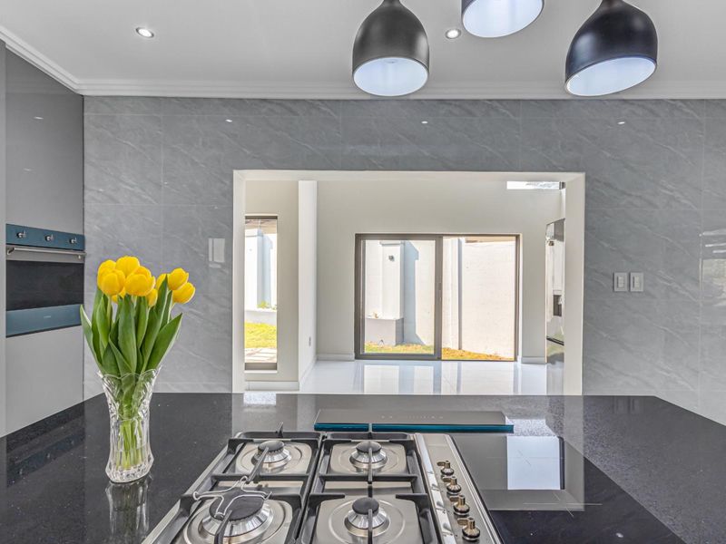 Modern kitchen featuring a sleek gas cooktop, built-in oven, stone countertops, and stylish pendant lighting, with a seamless transition to the outdoor area.