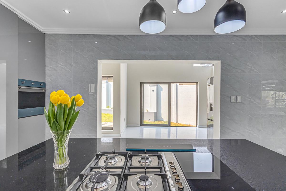 Modern kitchen featuring a sleek gas cooktop, built-in oven, stone countertops, and stylish pendant lighting, with a seamless transition to the outdoor area.