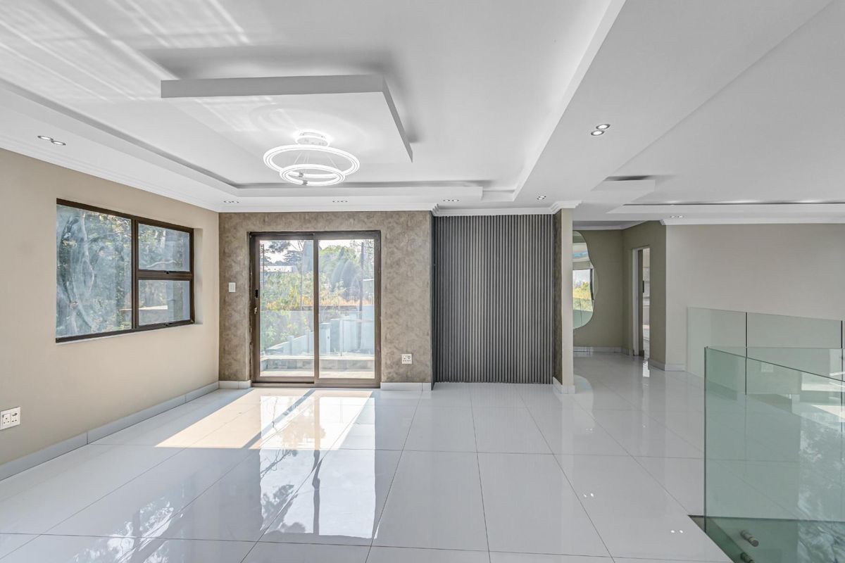 Spacious, modern living area featuring high-gloss tiled floors, a decorative slatted feature wall, recessed ceiling lighting, and a glass balustrade overlooking the lower level.