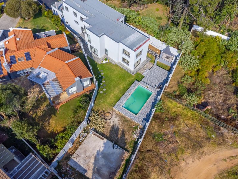 Aerial view of the property featuring a swimming pool, paved patio area, solar panels on the roof, and a large rear garden space.