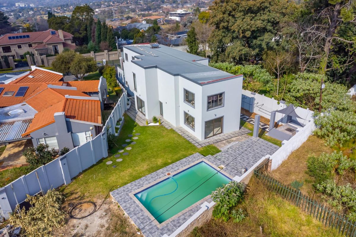 Aerial view of a modern double-story house featuring a swimming pool, paved patio area, and landscaped garden within a secure residential estate.
