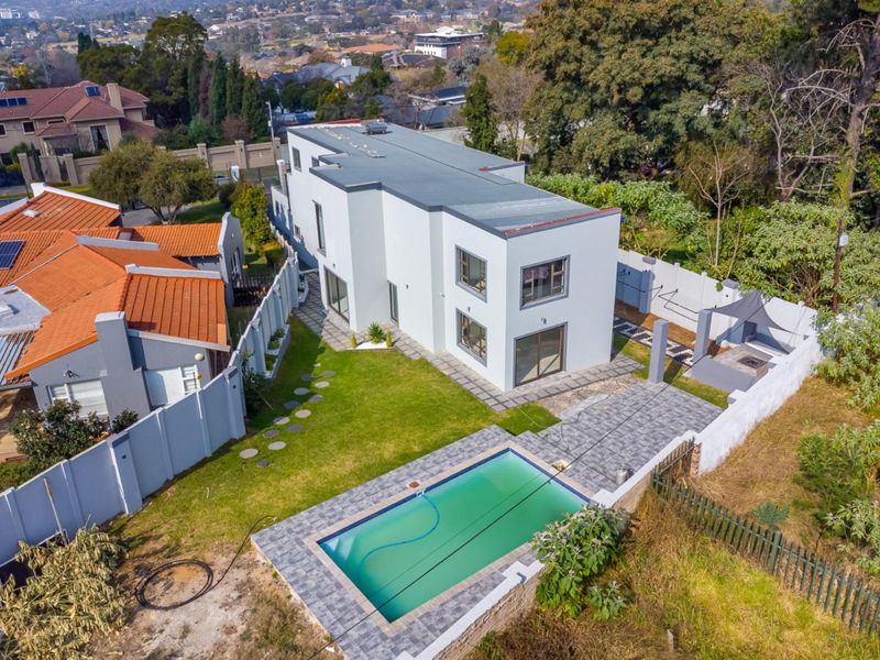 Aerial view of a modern double-story house featuring a swimming pool, paved patio area, and landscaped garden within a secure residential estate.