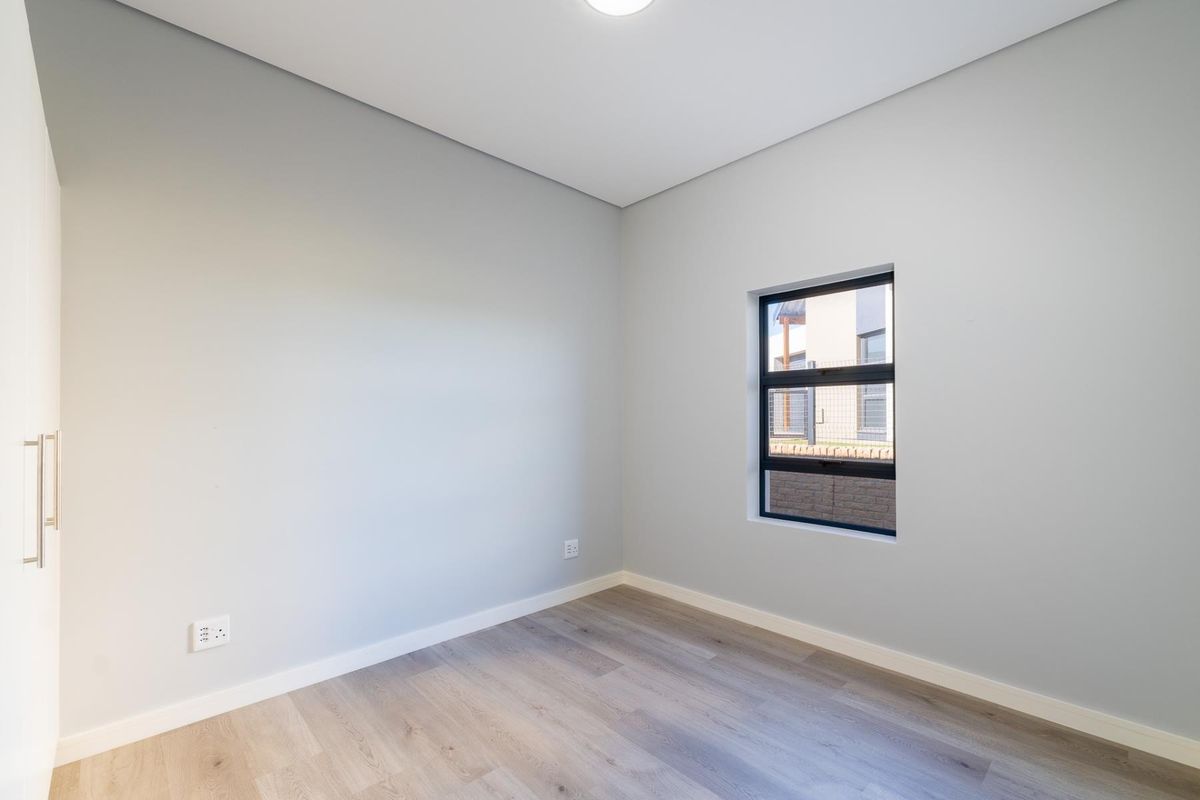 A bright, modern bedroom featuring neutral walls, light wood-look flooring, and a built-in wardrobe.