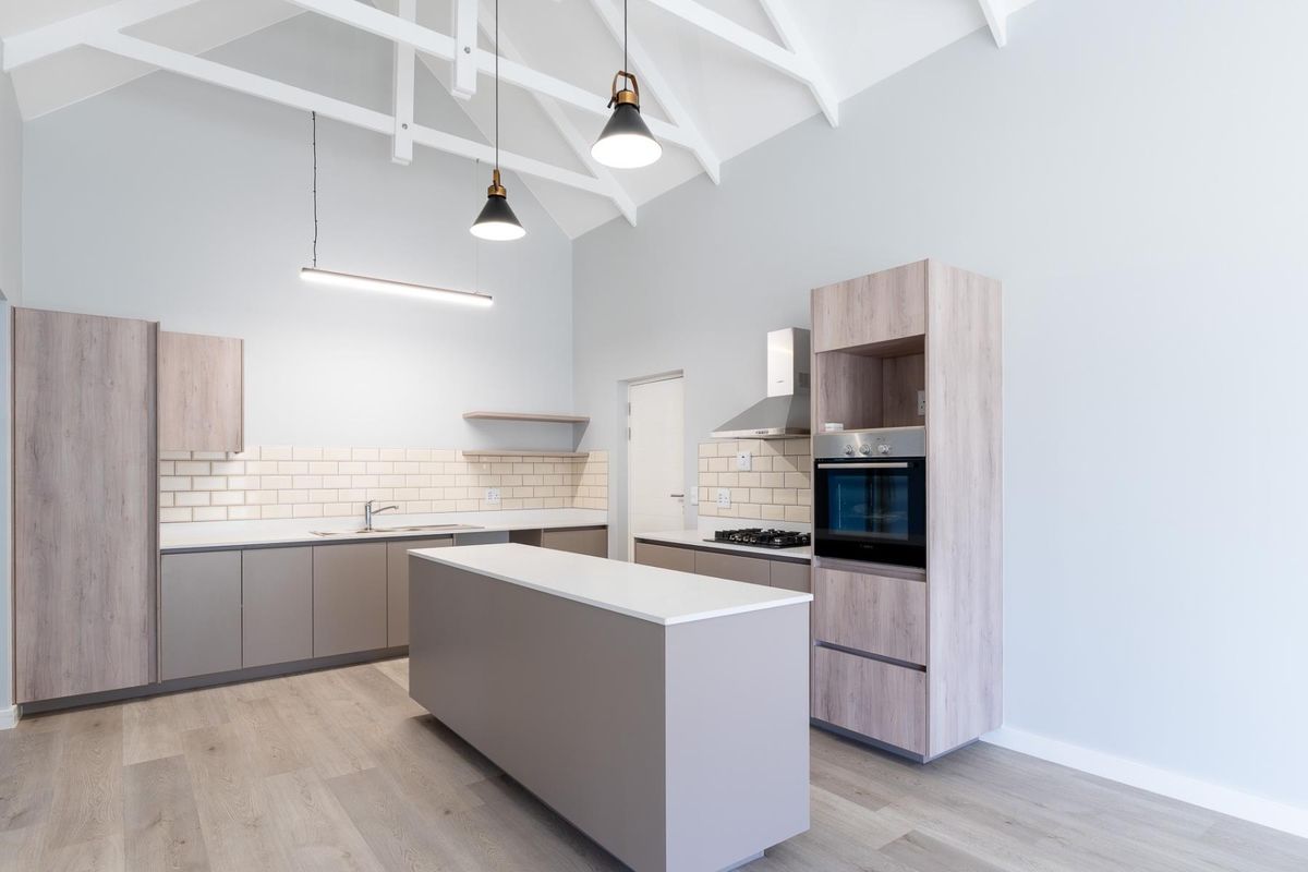 Modern kitchen featuring a central island, built-in oven, gas hob, extractor fan, and subway tile backsplash under a high vaulted ceiling.