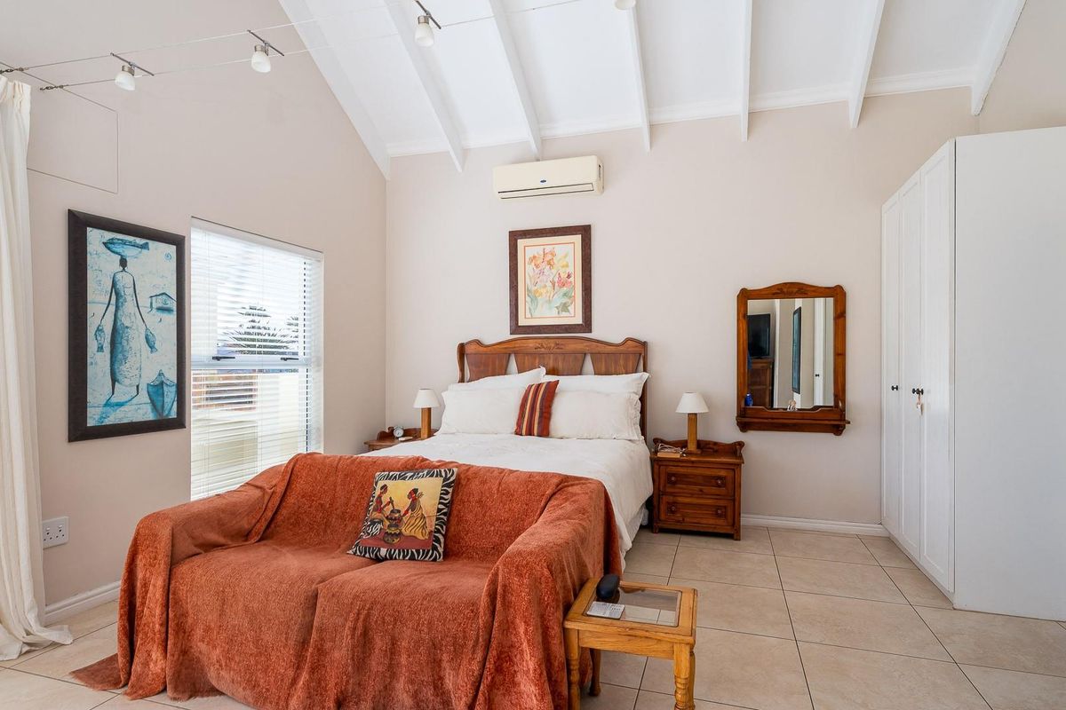 A bedroom featuring a vaulted ceiling with exposed beams, tiled flooring, built-in wardrobe, and a wall-mounted air conditioning unit.