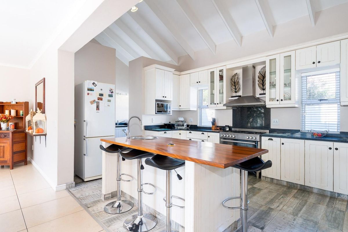 A bright kitchen featuring white cabinetry, a wooden breakfast island with a built-in sink, and a vaulted ceiling with exposed beams.