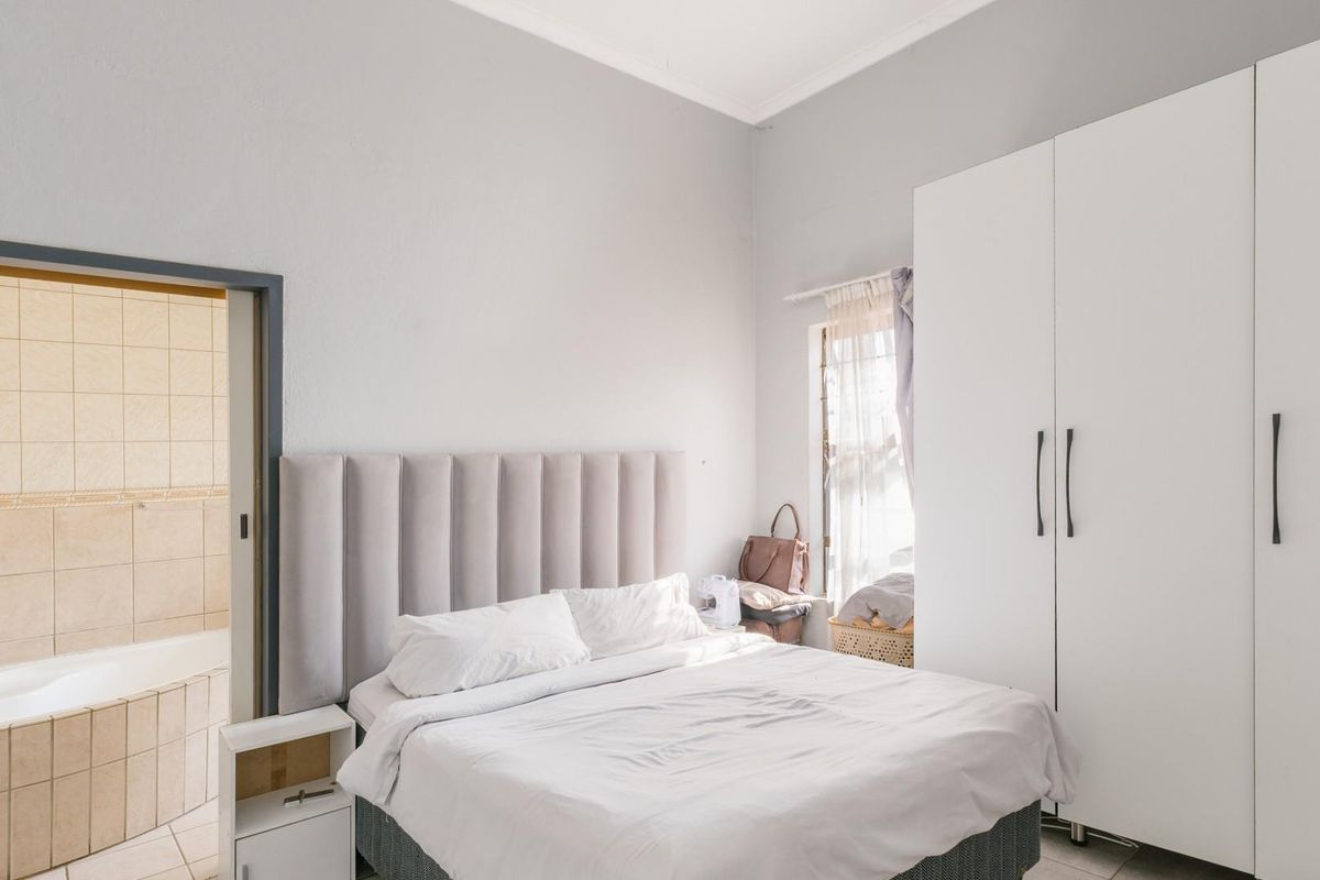 A bedroom featuring built-in white wardrobes and an adjoining bathroom with tiled walls and a bathtub.