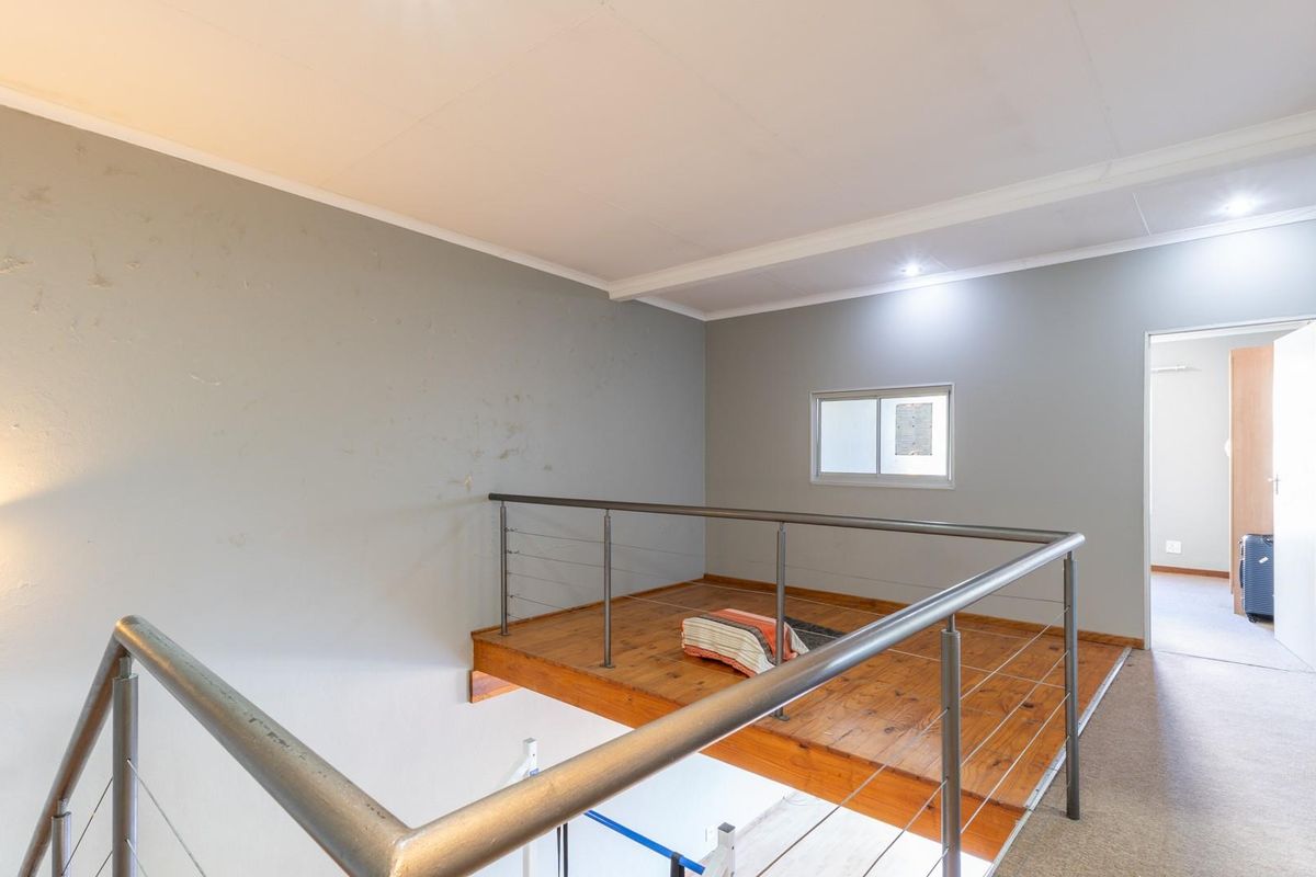 A mezzanine level overlooking the lower floor, featuring timber flooring, a stainless steel balustrade, and neutral wall finishes.