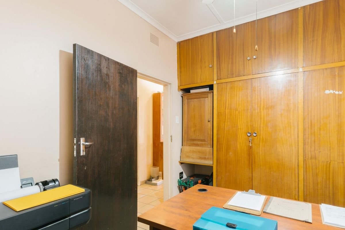 A functional bedroom or office space featuring extensive floor-to-ceiling built-in wooden cabinetry and a solid timber door.
