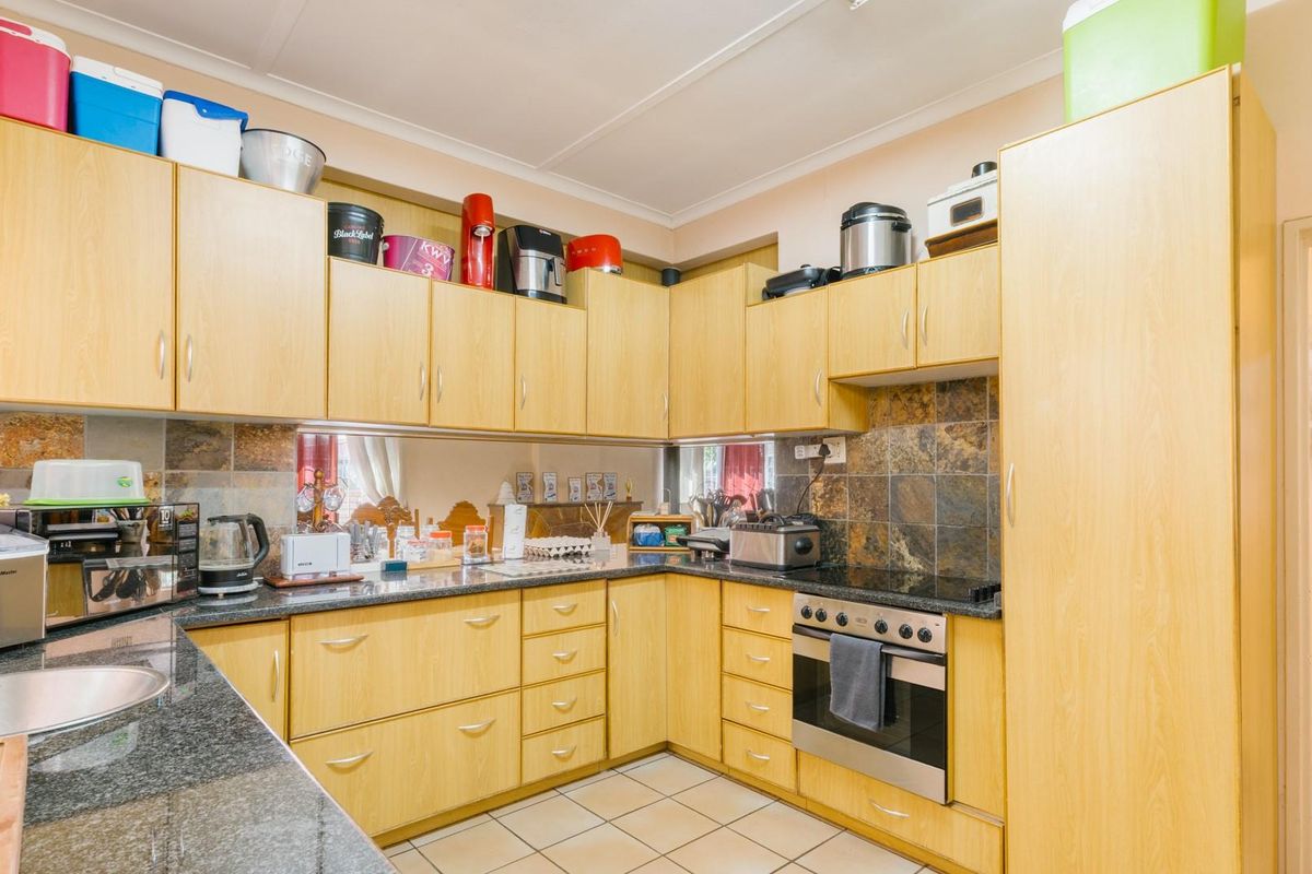 A functional kitchen featuring light wood-finish cabinetry, granite countertops, a built-in oven with hob, and slate-style tiled splashbacks.