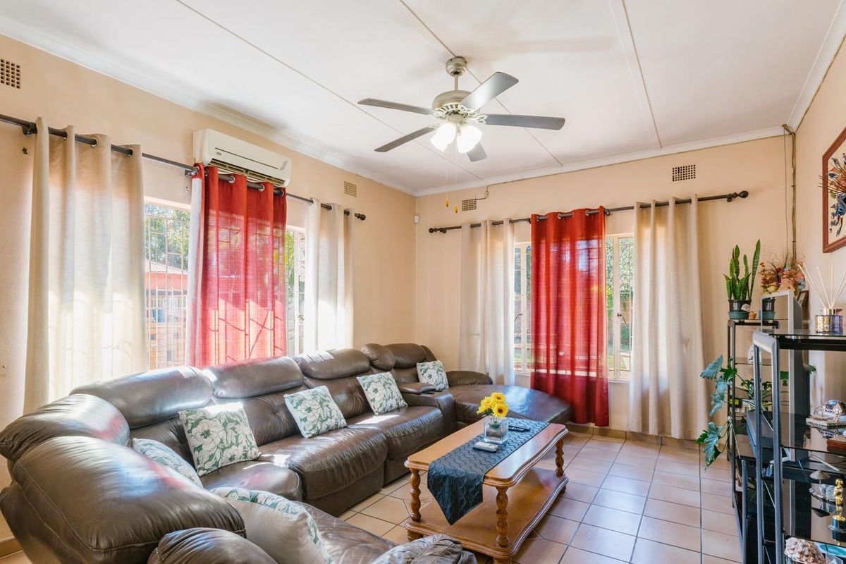 A comfortable living room featuring tiled flooring, a ceiling fan, and a wall-mounted air conditioning unit, providing a functional and well-lit living space.