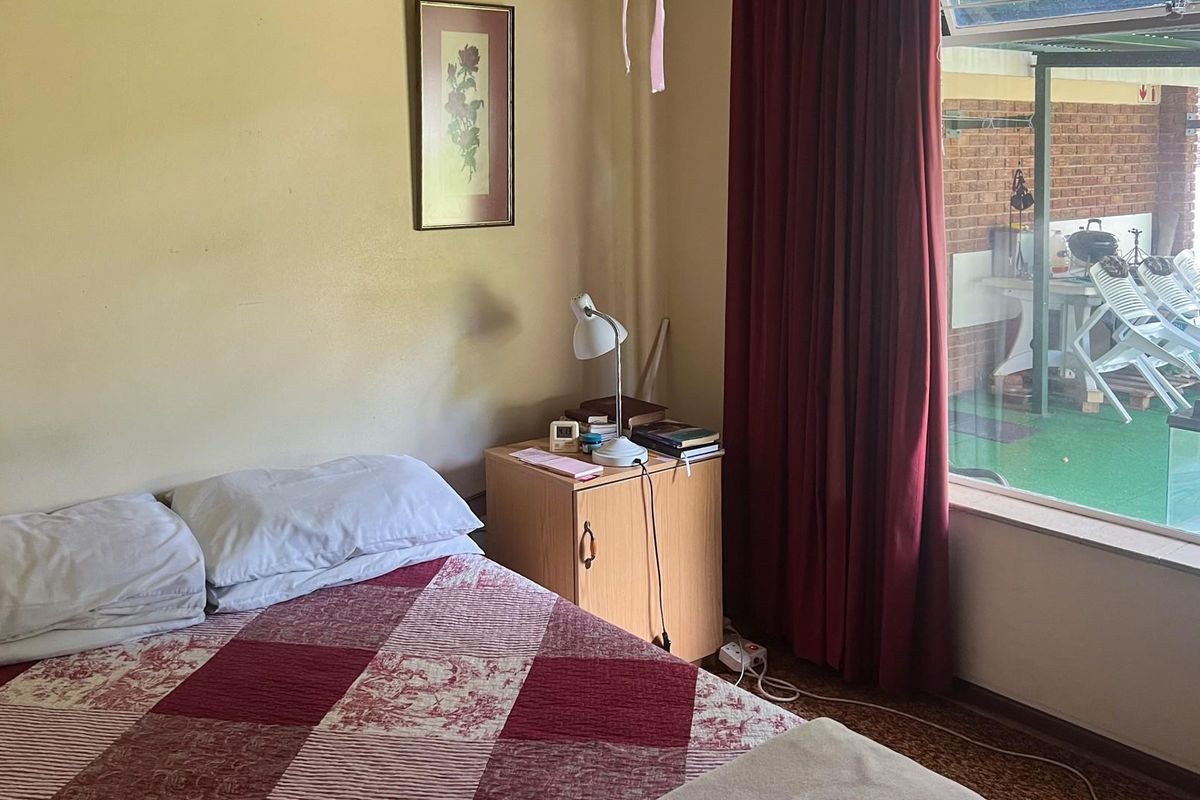 A bedroom featuring a large window with views of an outdoor patio area, finished with neutral wall paint and carpeted flooring.