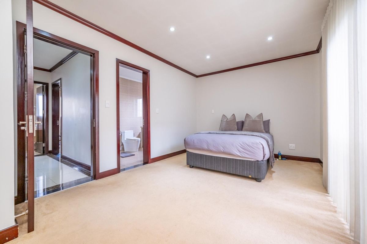 Spacious bedroom featuring neutral carpeting, dark wood trim, recessed lighting, and an en-suite bathroom with tiled finishes.