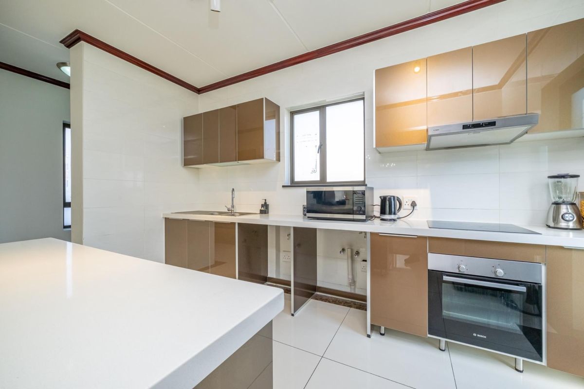 Modern kitchen featuring high-gloss cabinetry, white stone countertops, integrated oven, and hob, with tiled flooring and clean finishes throughout.