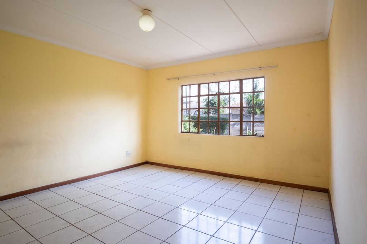 An empty bedroom featuring tiled flooring, yellow painted walls, and a large window with a grid pattern.