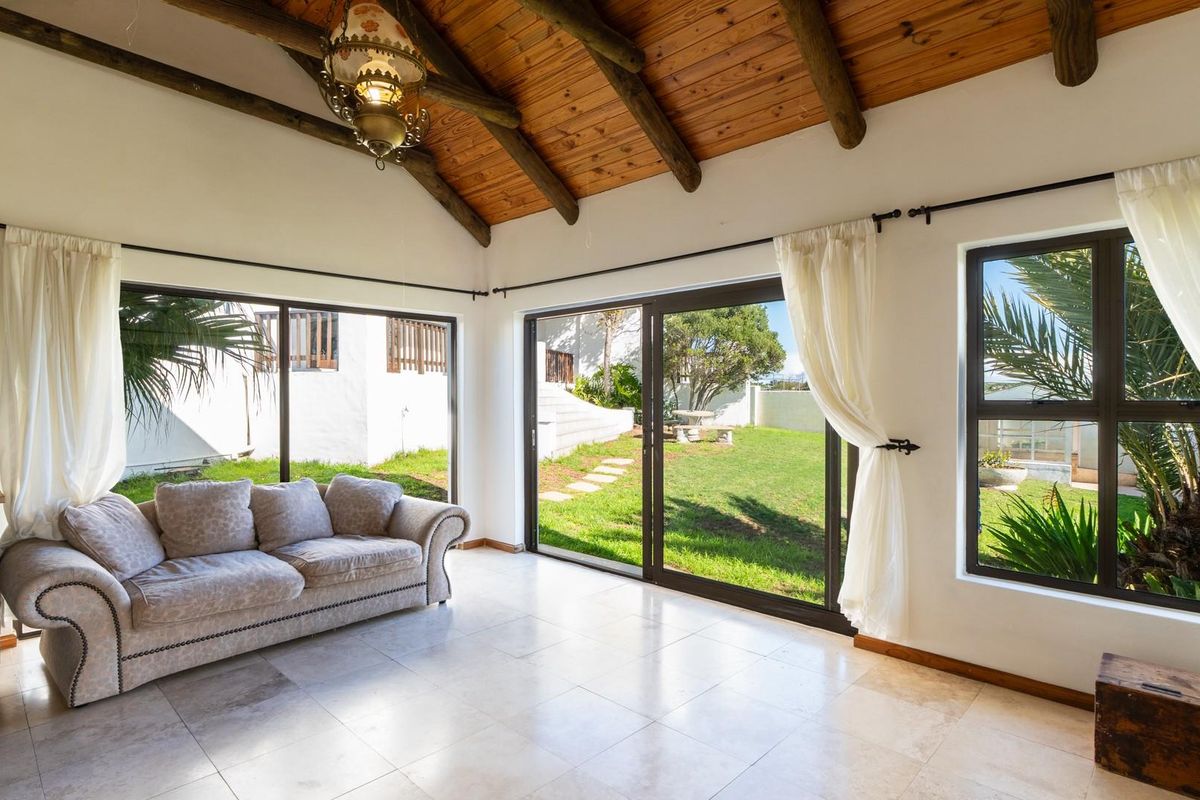Bright living area featuring exposed timber beam vaulted ceilings, large sliding glass doors, and tiled flooring with direct access to the garden.