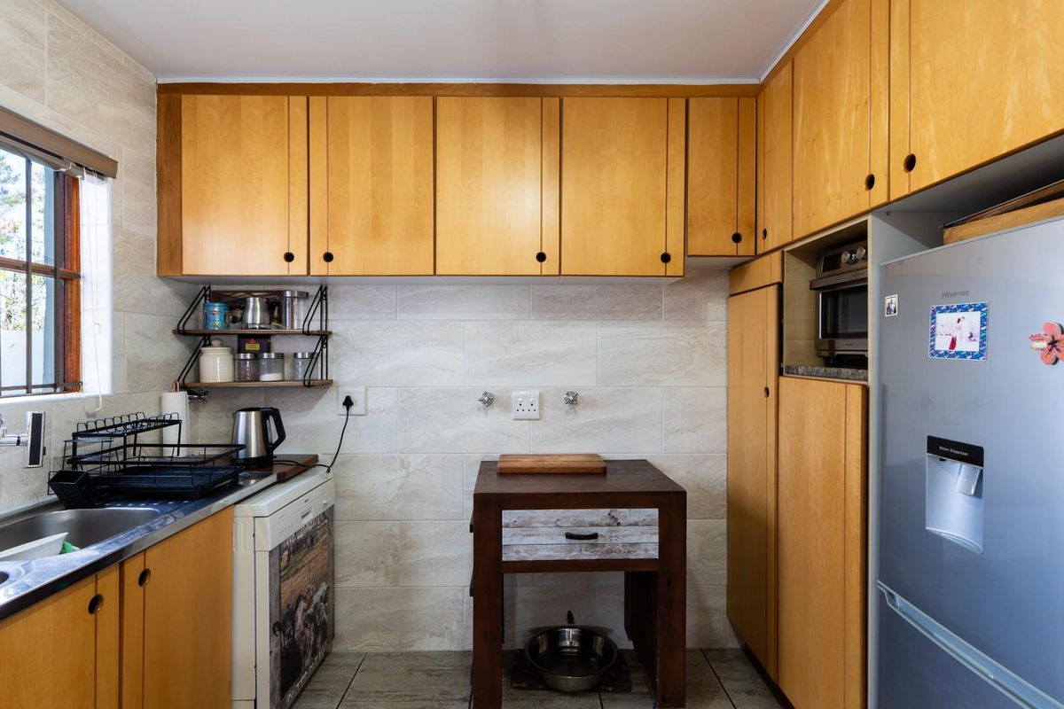 A functional kitchen featuring light wood cabinetry, tiled backsplash, stainless steel sink, and integrated appliance space with natural light from a side window.