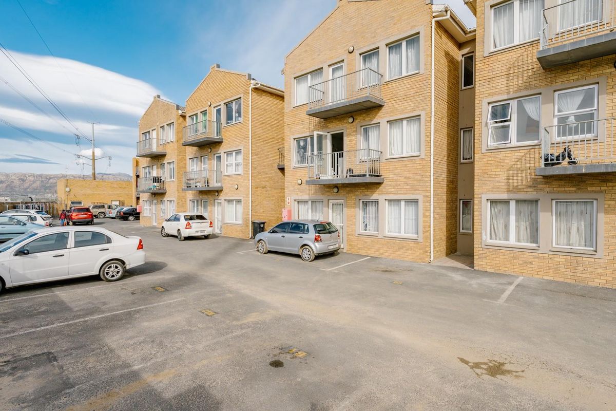 Exterior view of a multi-story brick apartment complex featuring private balconies and dedicated paved parking spaces.