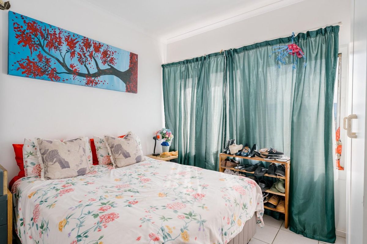 A bedroom featuring tiled flooring and large windows covered by curtains, providing natural light to the space.