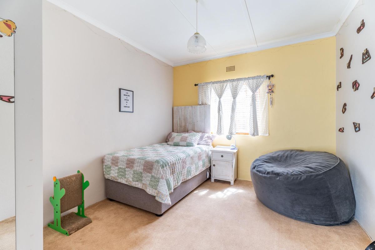 A standard bedroom featuring neutral wall tones, a yellow accent wall, carpeted flooring, and a window with natural light.